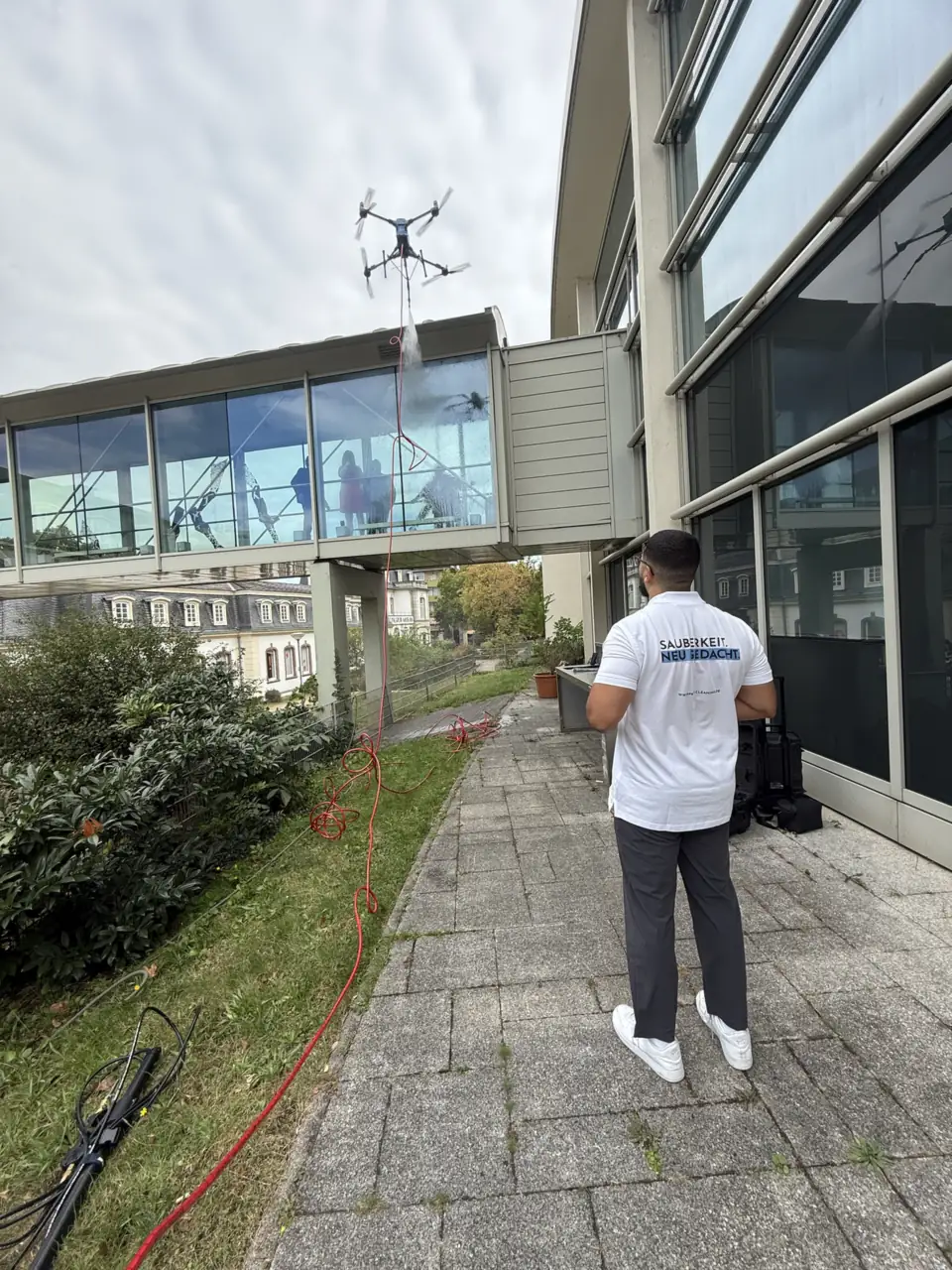 Reinigungsdrohne an einem verglasten Übergang, der Pilot steuert vom Boden aus