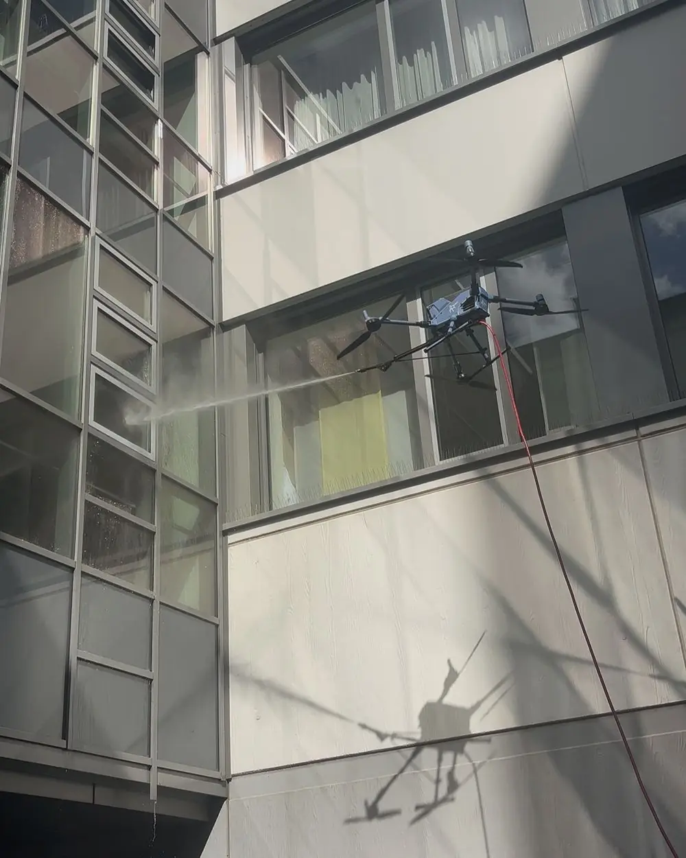 Reinigungsdrohne spült eine Glasfassade, ihr Schatten fällt auf die Wand darunter